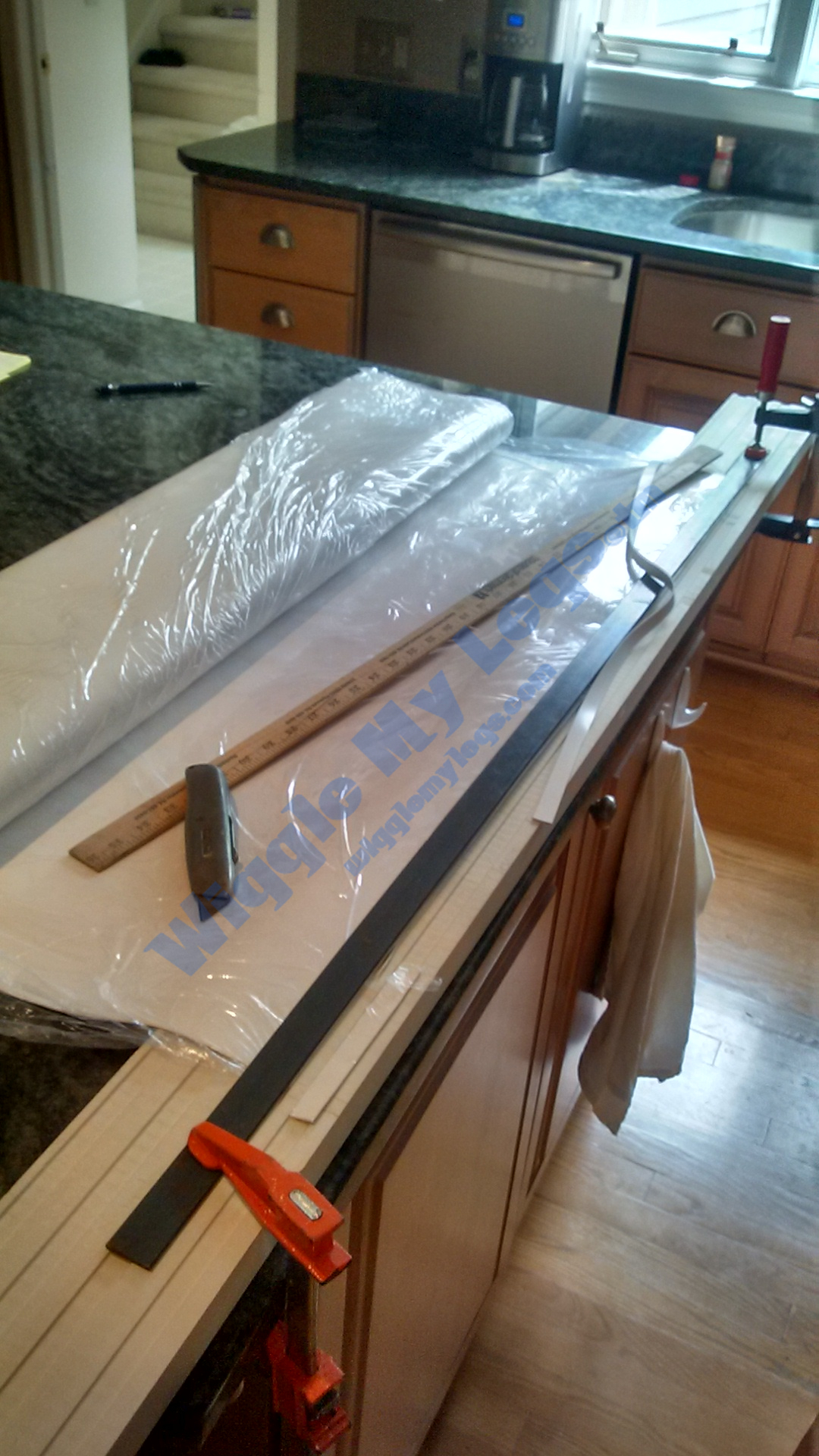 View of the dark metal straight edge clamped onto rubber sheet to allow utility knife to cut straight strips for new stove seals under spill trays.